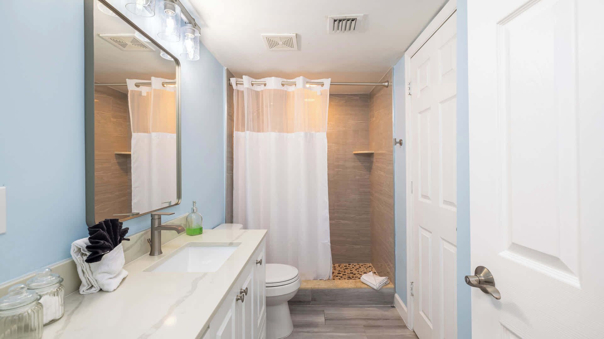 A compact bathroom with a white sink, a mirror, a toilet, and a shower area.