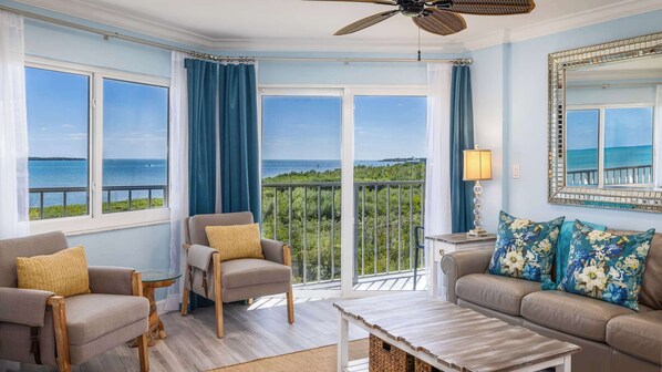 Un salon spacieux avec vue sur la mer, un ventilateur de plafond et un grand miroir.