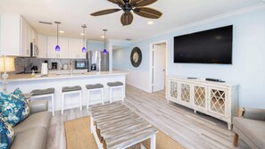 A modern living room with a kitchen area, a dining bar, and a large flat-screen TV. - Ocean View Treehouse Double King Suite 3403 (Tavernier)