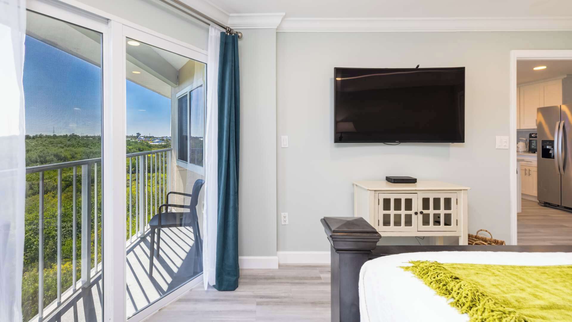 Quarto de hotel moderno com varanda, televisão de tela plana, um pequeno armário e uma cama com manta verde.