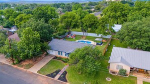 A residential area with a swimming pool, a covered patio, and a well-maintained lawn. - Boho Bougie: Pool, Hot Tub & Epic Back Yard (Fredericksburg)