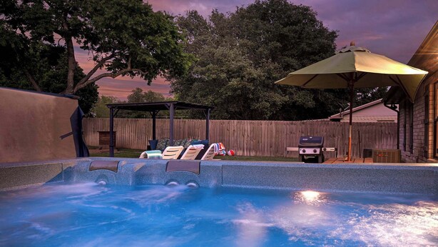 A hot tub with a wooden deck, a covered seating area, and a wooden fence in the background. - Boho Bougie: Pool, Hot Tub & Epic Back Yard (Fredericksburg)