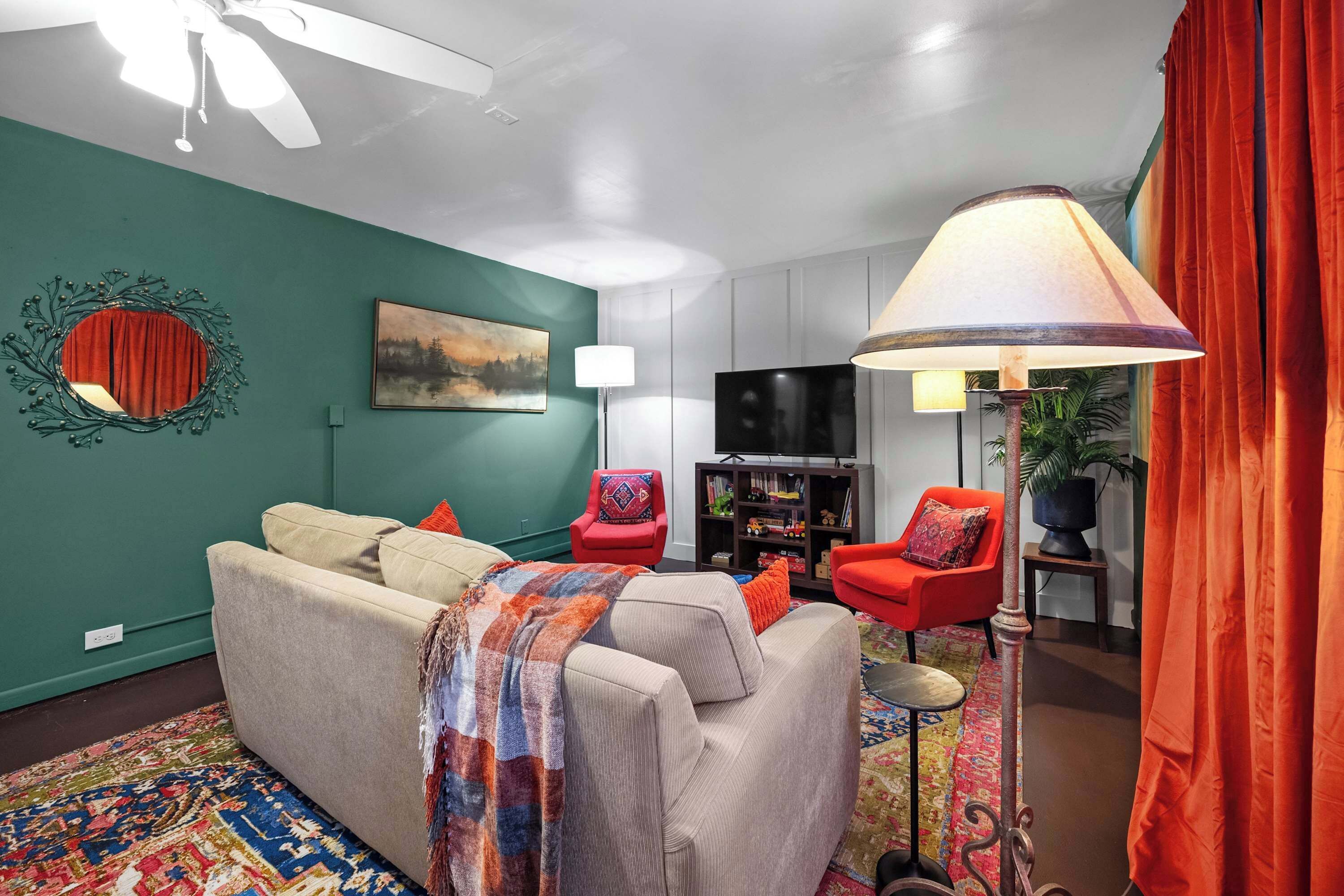 A living room with a sofa, red chairs, a TV, and a lamp.