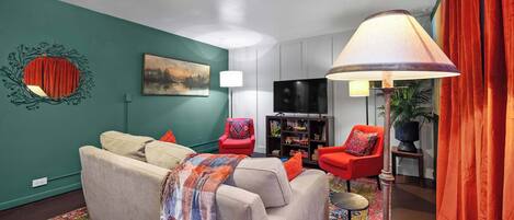A living room with a sofa, red chairs, a TV, and a lamp.