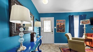 A room with a blue wall, a white door, a blue console table with a lamp, a yellow armchair, and a colorful rug. - Boho Bougie: Pool, Hot Tub & Epic Back Yard (Fredericksburg)