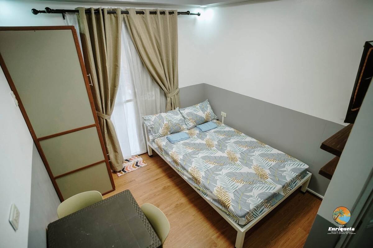 A small, single-bed room with a wooden floor, a desk, and a chair.
