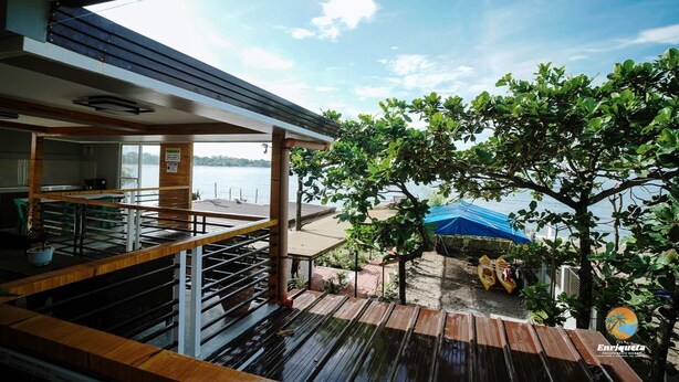 Una terraza de madera con vista a un lago, un árbol y una tienda de campaña azul.
