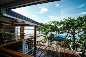 Una terraza de madera con vista a un lago, un árbol y una tienda de campaña azul.