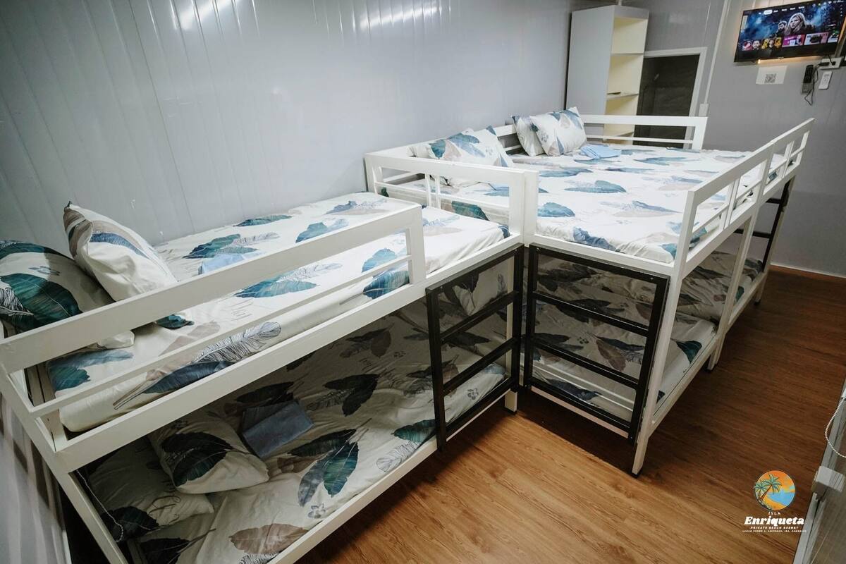A room with bunk beds, wooden flooring, and a TV on the wall.