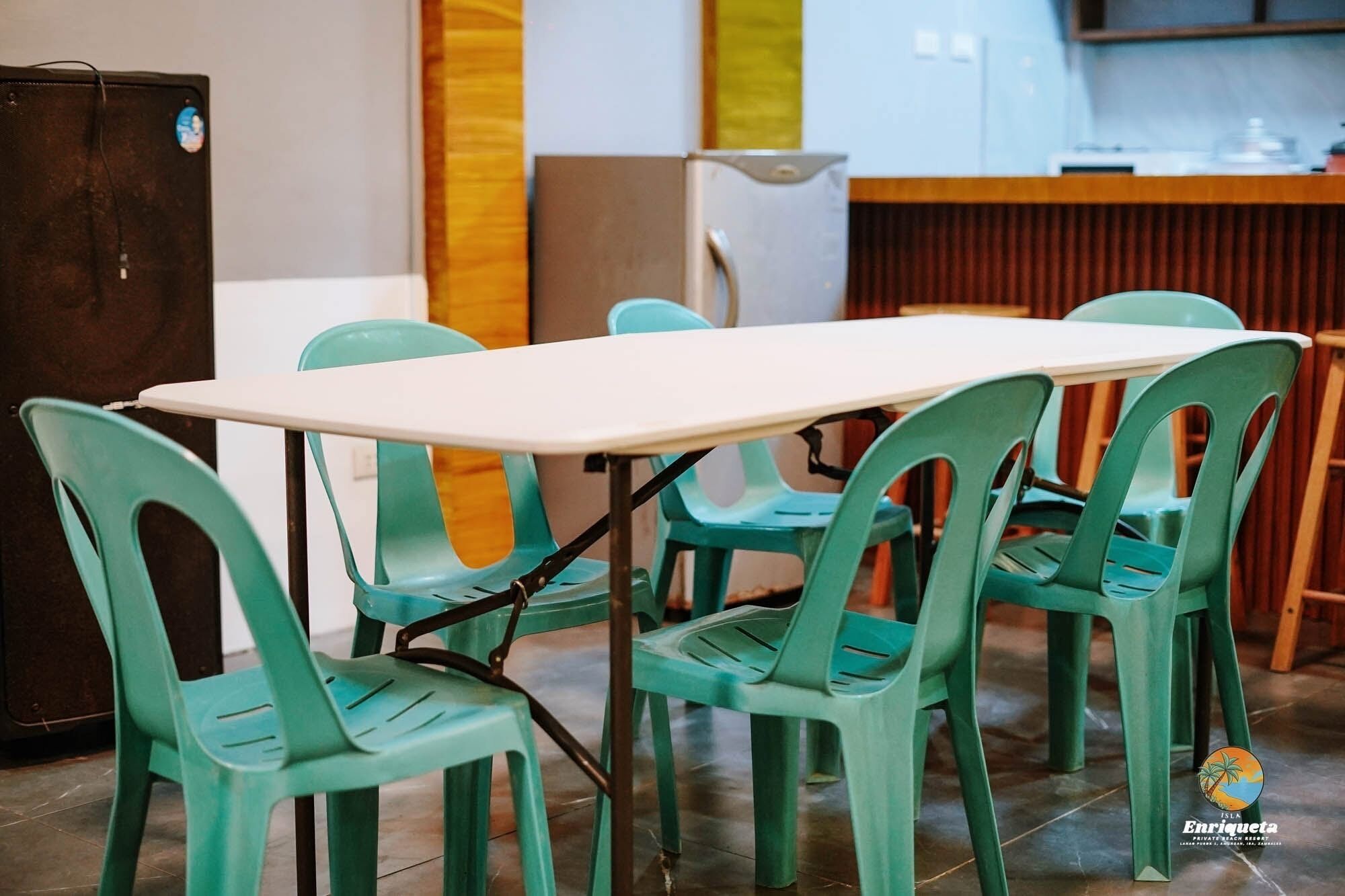 Een eethoek met een witte tafel en groene stoelen, een koelkast en een keuken in de achtergrond.
