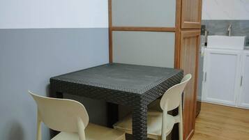 A small dining area with a table and two chairs, a wooden cabinet, and a kitchenette in the background.