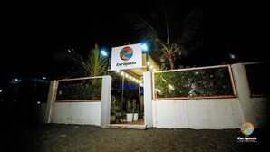 Entrada de un resort privado en la playa, con letrero, palmeras y acceso mediante portón.