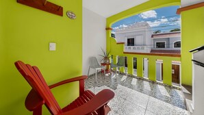 Habitació lluminosa amb una cadira vermella, una taula petita i una planta en test. Hi ha una finestra amb vista a un edifici a l'exterior.