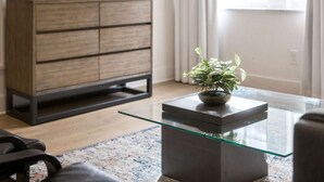 A modern living room with a glass-top coffee table, a dark wooden cabinet, and a potted plant.