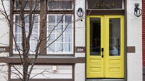 A building with a yellow door, the number 1224 above it, and a tree in front.