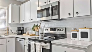 Una cocina moderna con armarios blancos, estufa de acero inoxidable, microondas y cafetera.