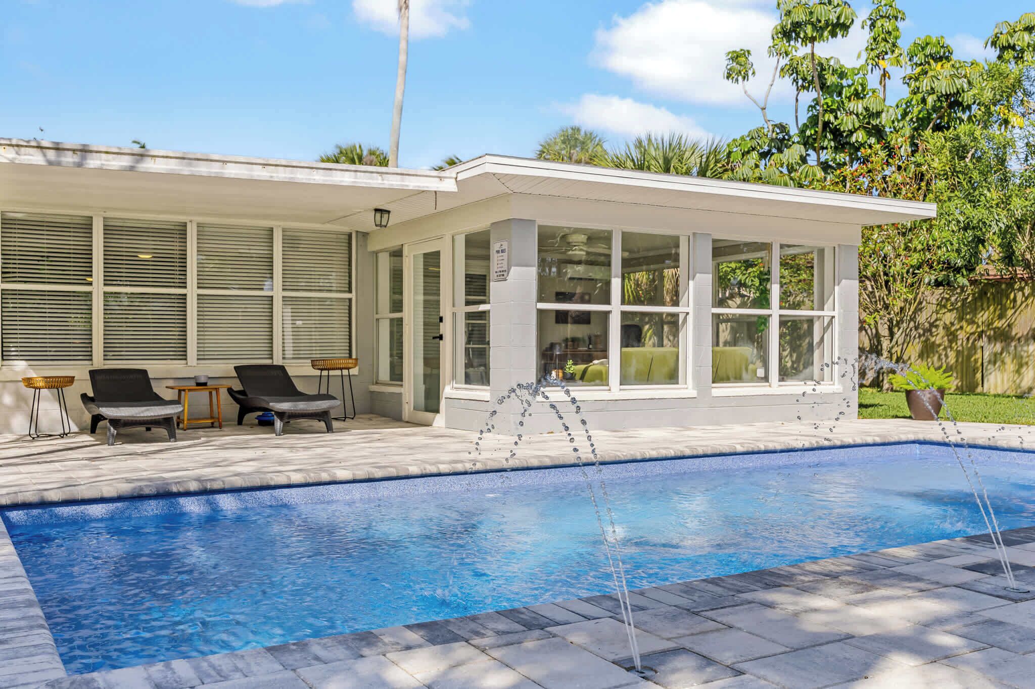 Modern patio area with lounge chairs overlooking a private pool with water fountains.