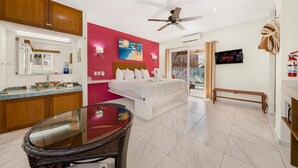 A hotel room with a bed, a glass-top table, a ceiling fan, a TV, and a view of the outdoors. - 1BR Studio downtown w/private rooftop outdoor soaking tub (Isla Mujeres)