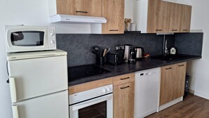 A compact kitchen with wooden cabinets, a white refrigerator, a microwave, a stove, and a dishwasher. - Apartment in the center of Guérande 4 minutes walk from the ramparts (Guérande)