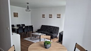 A modern living room with a black patterned sofa, a round wooden coffee table, and a dining area with a white table and black chairs. - Apartment in the center of Guérande 4 minutes walk from the ramparts (Guérande)