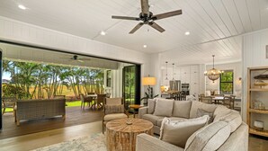 A spacious living room with a large sofa, a round coffee table, and a view of the outdoors. - Hale Kohola by Alekona Kauai: Brand New 4BR Home w AC, close to beaches, shopping, dining (Koloa)