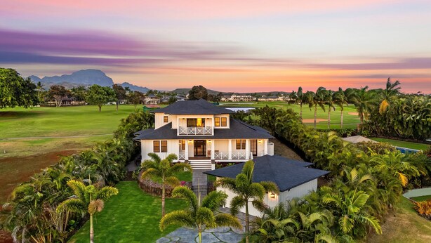 A two-story house with a front porch, surrounded by lush greenery and a golf course in the background. - Hale Kohola by Alekona Kauai: Brand New 4BR Home w AC, close to beaches, shopping, dining (Koloa)