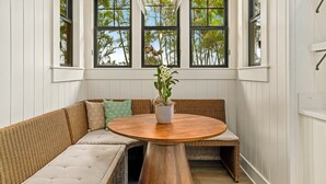 A room with a round wooden table, wicker sofa, and a potted plant. - Hale Kohola by Alekona Kauai: Brand New 4BR Home w AC, close to beaches, shopping, dining (Koloa)