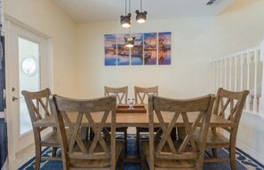 A dining area with a wooden table and chairs, a decorative ceiling light, and a cityscape painting on the wall. - Family-Friendly 5BR with BBQ & Resort Perks (Clermont)