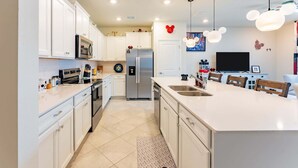 A modern kitchen with white cabinets, stainless steel appliances, a central island, and Mickey Mouse-themed decor. - Family-Friendly 5BR with BBQ & Resort Perks (Clermont)