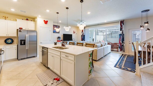 A modern kitchen with a central island, stainless steel appliances, and a dining area with a view. - Family-Friendly 5BR with BBQ & Resort Perks (Clermont)