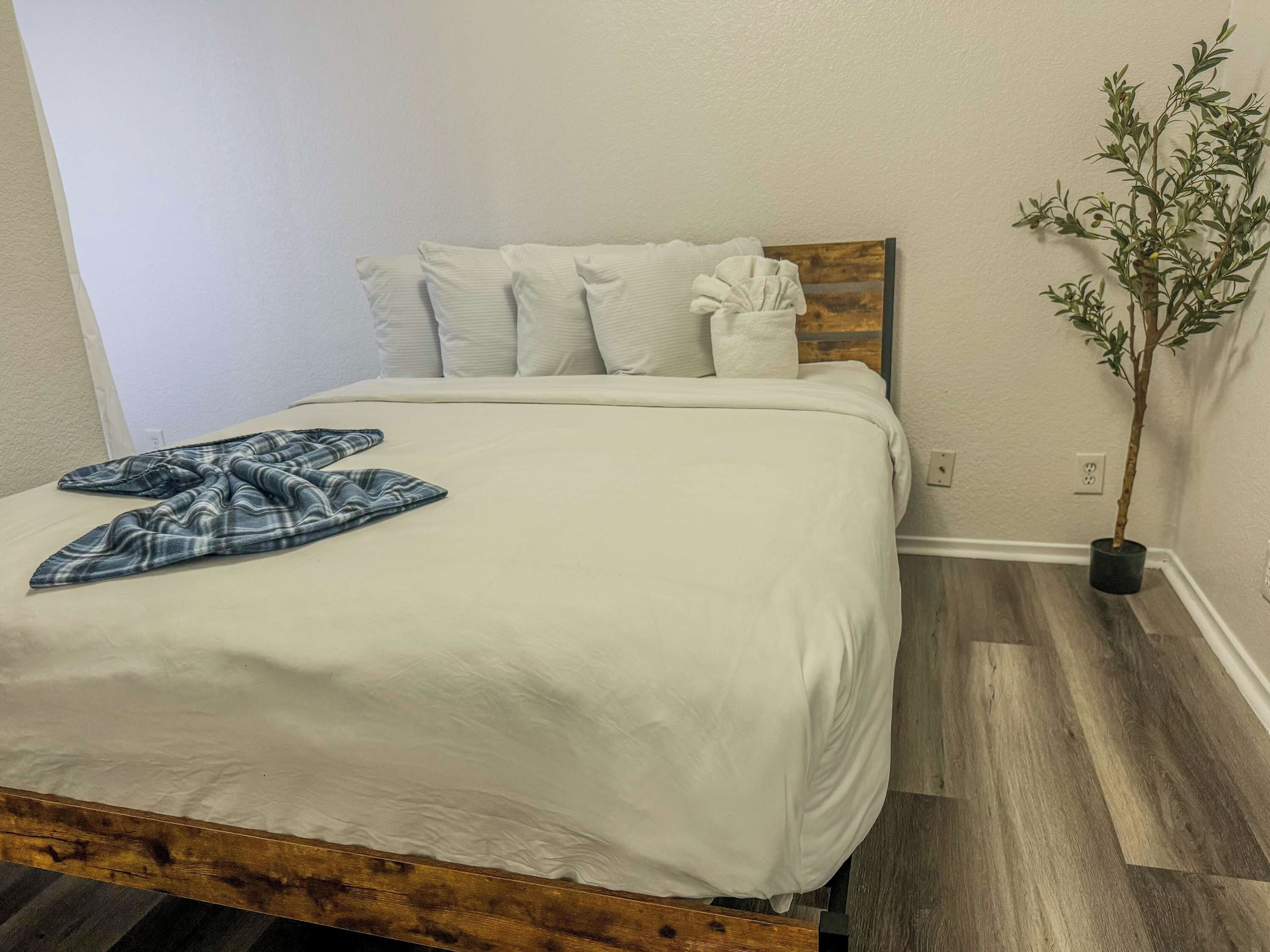 A bed with white bedding, a wooden headboard, and a blue plaid blanket.