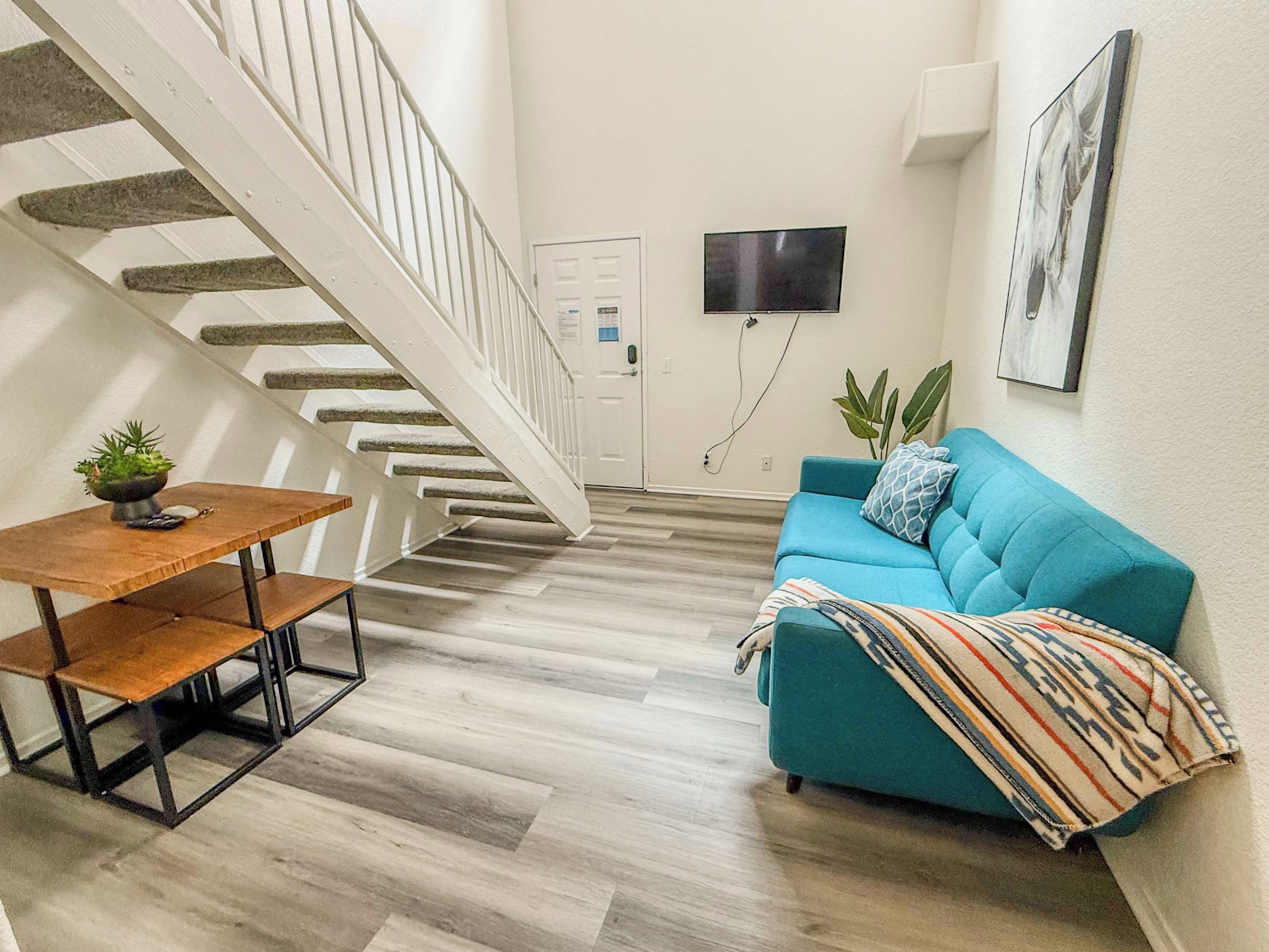 A staircase leading to a door, a blue sofa with a patterned throw, and a small table with a plant.