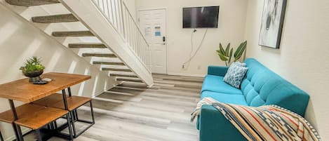 A staircase leading to a door, a blue sofa with a patterned throw, and a small table with a plant.