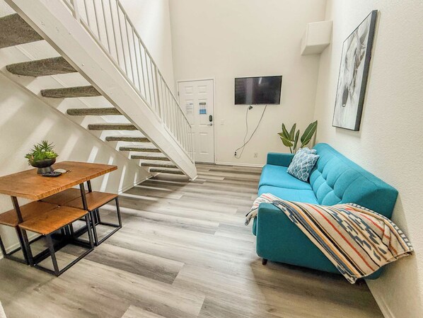 A staircase leading to a door, a blue sofa with a patterned throw, and a small table with a plant.