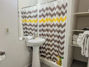 A bathroom with a shower curtain featuring a zigzag pattern, a white sink, and a towel rack with folded towels.