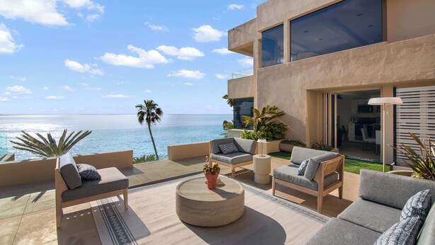 A modern outdoor living area with a view of the ocean, featuring a sofa set, a round coffee table, and potted plants. - La Jolla Suite with Ocean View Patio (San Diego)