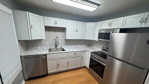 Cozinha moderna com armários brancos, geladeira de aço inoxidável, micro-ondas e forno.