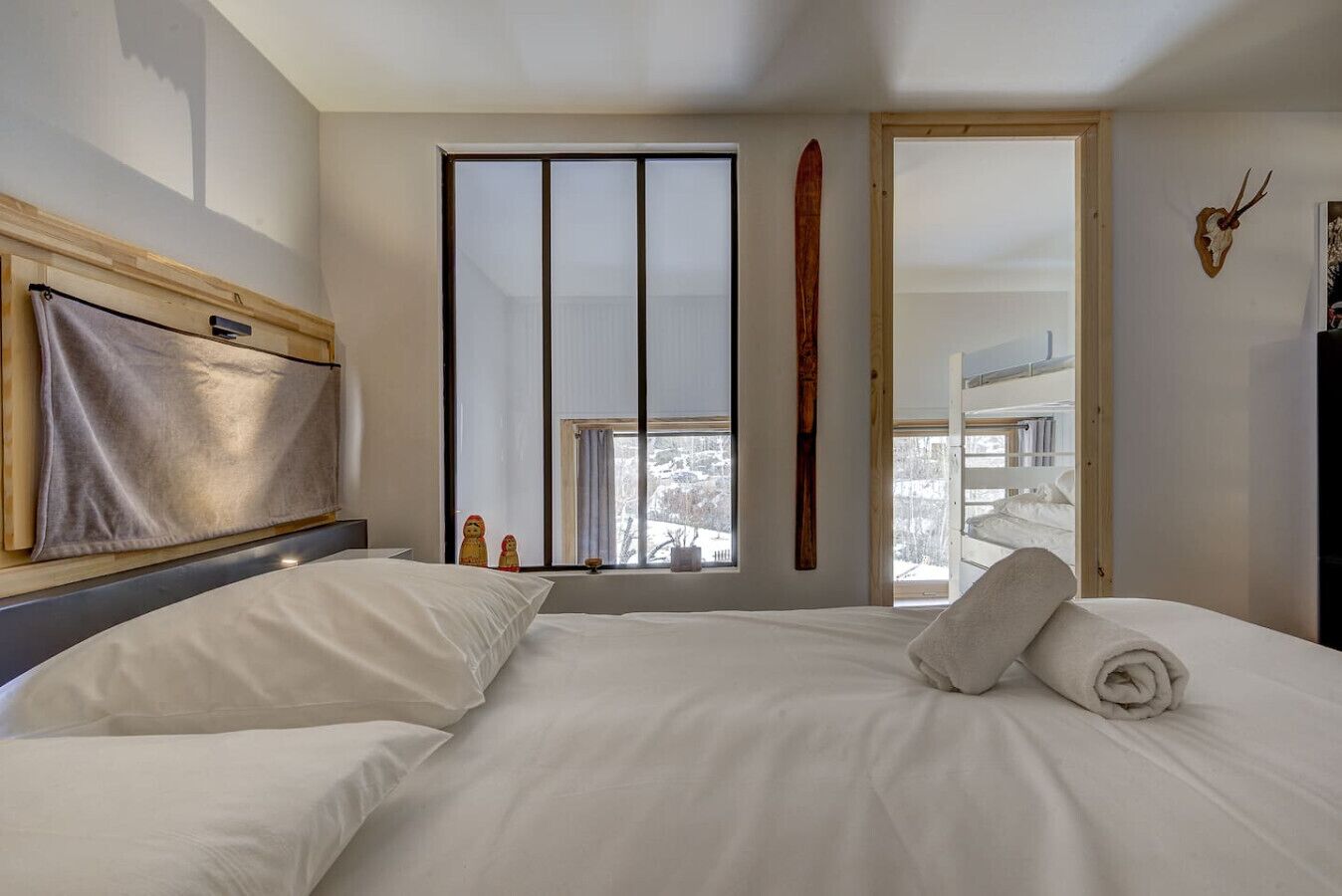 Una habitación de hotel con una cama grande, cabecera de madera, un esquí en la pared y vistas a un paisaje nevado.