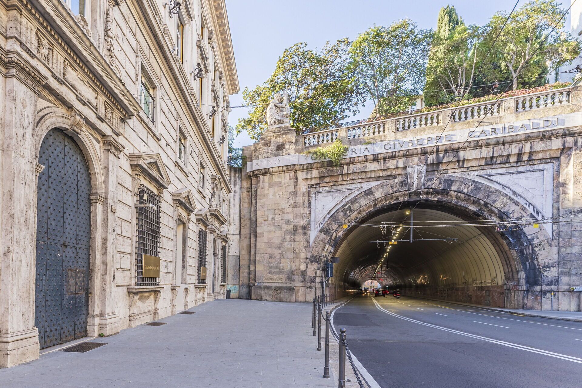A tunnel entrance with an arched stone structure, a metal gate, and a sidewalk leading to it.