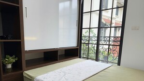 Une chambre à coucher comprenant un lit, une armoire, une petite table avec une plante et une fenêtre donnant sur un balcon.