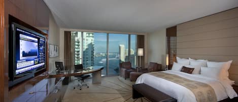 A hotel room with a large bed, a desk, a TV, and a view of the city.