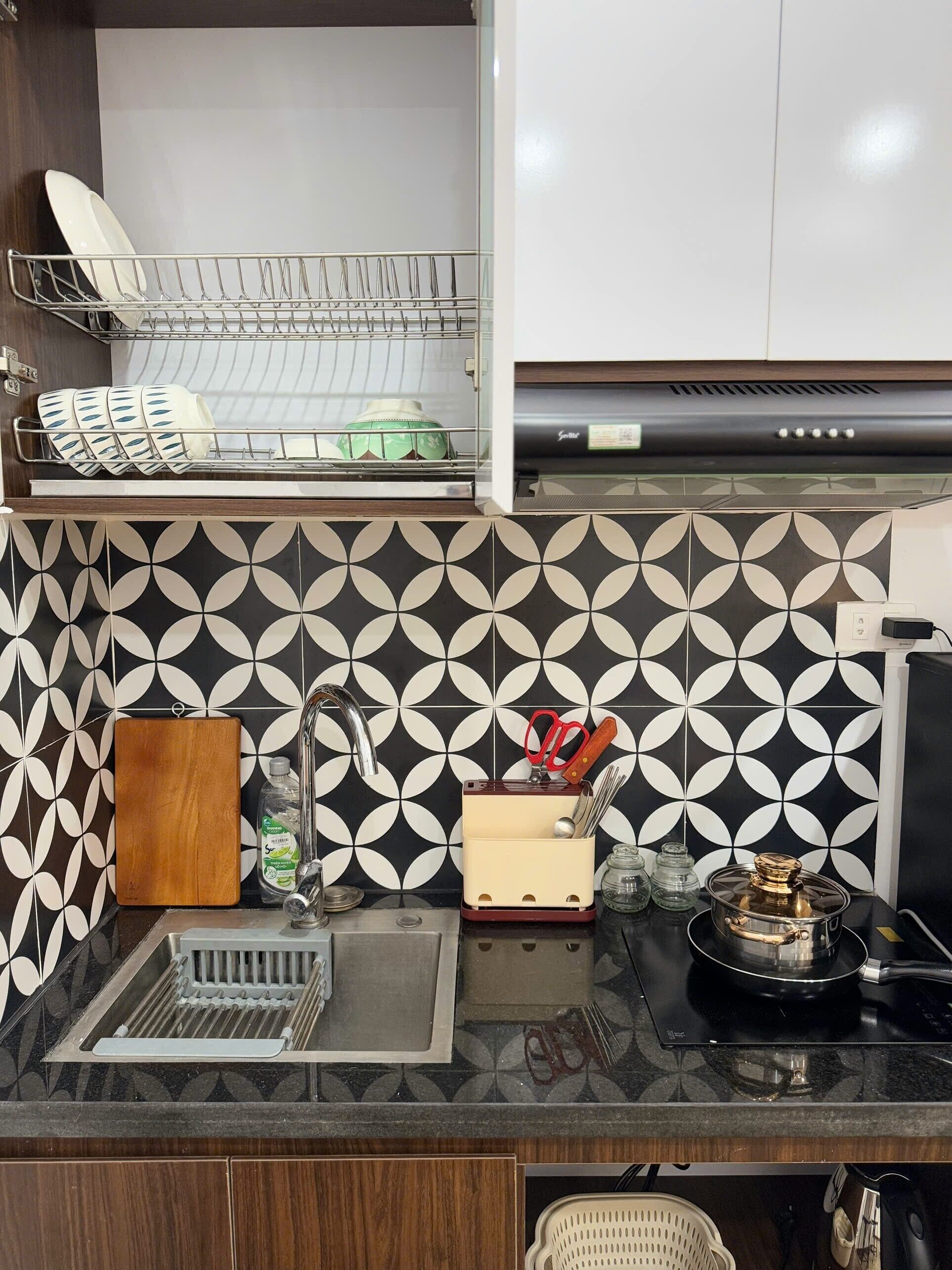 Une cuisine avec un plan de travail noir et blanc à motifs, un égouttoir à vaisselle, une planche à découper, un évier et une cuisinière.