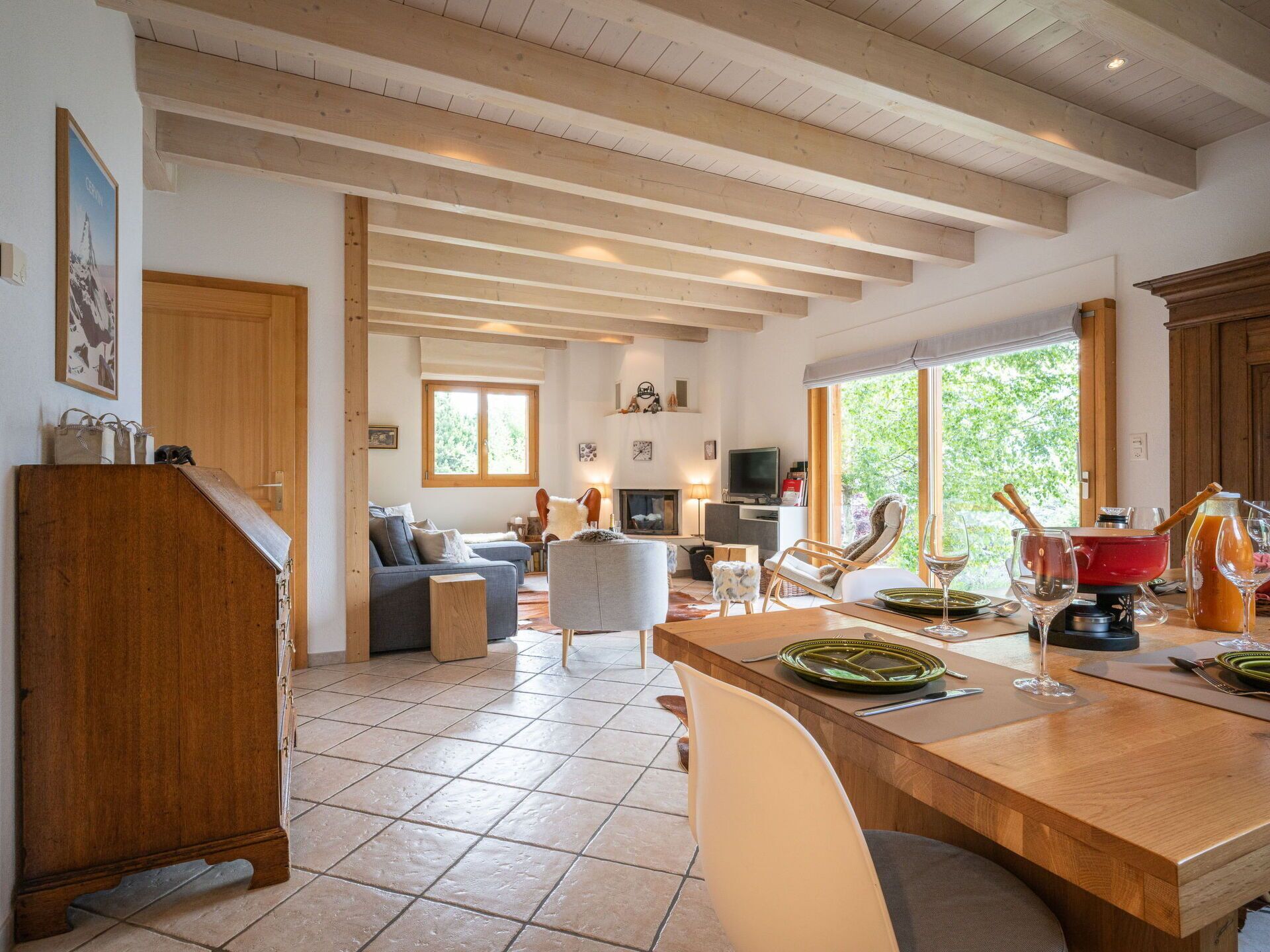 Un vaste espace de vie avec un plafond en bois, une table à manger dressée avec des assiettes et des verres, et un téléviseur en arrière-plan.