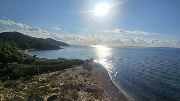 A coastal landscape with a clear sky, calm sea, and rocky terrain.