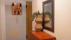 A hallway with a wooden console table, two woven baskets with plants, a wall-mounted mirror, and a door with a wooden frame.