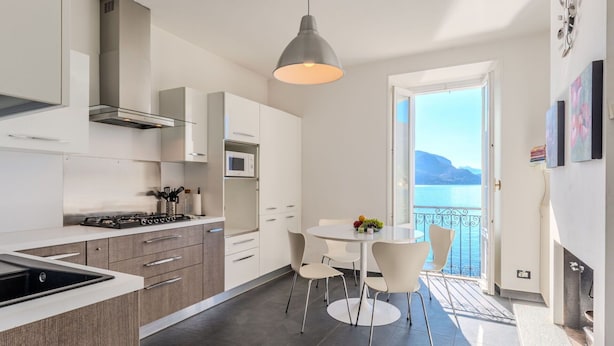 A modern kitchen with a gas stove, microwave, and white cabinets. There is a dining area with a table and chairs, and a balcony with a view of the sea. - Lovely apartment for 6 people with WIFI and TV (San Siro)