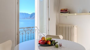 A room with a balcony overlooking a body of water and mountains, a table with fruit, a chair, and a radiator. - Lovely apartment for 6 people with WIFI and TV (San Siro)
