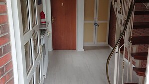 Un couloir avec une porte en bois, un escalier doté d’une rampe en métal et une moquette bleue.