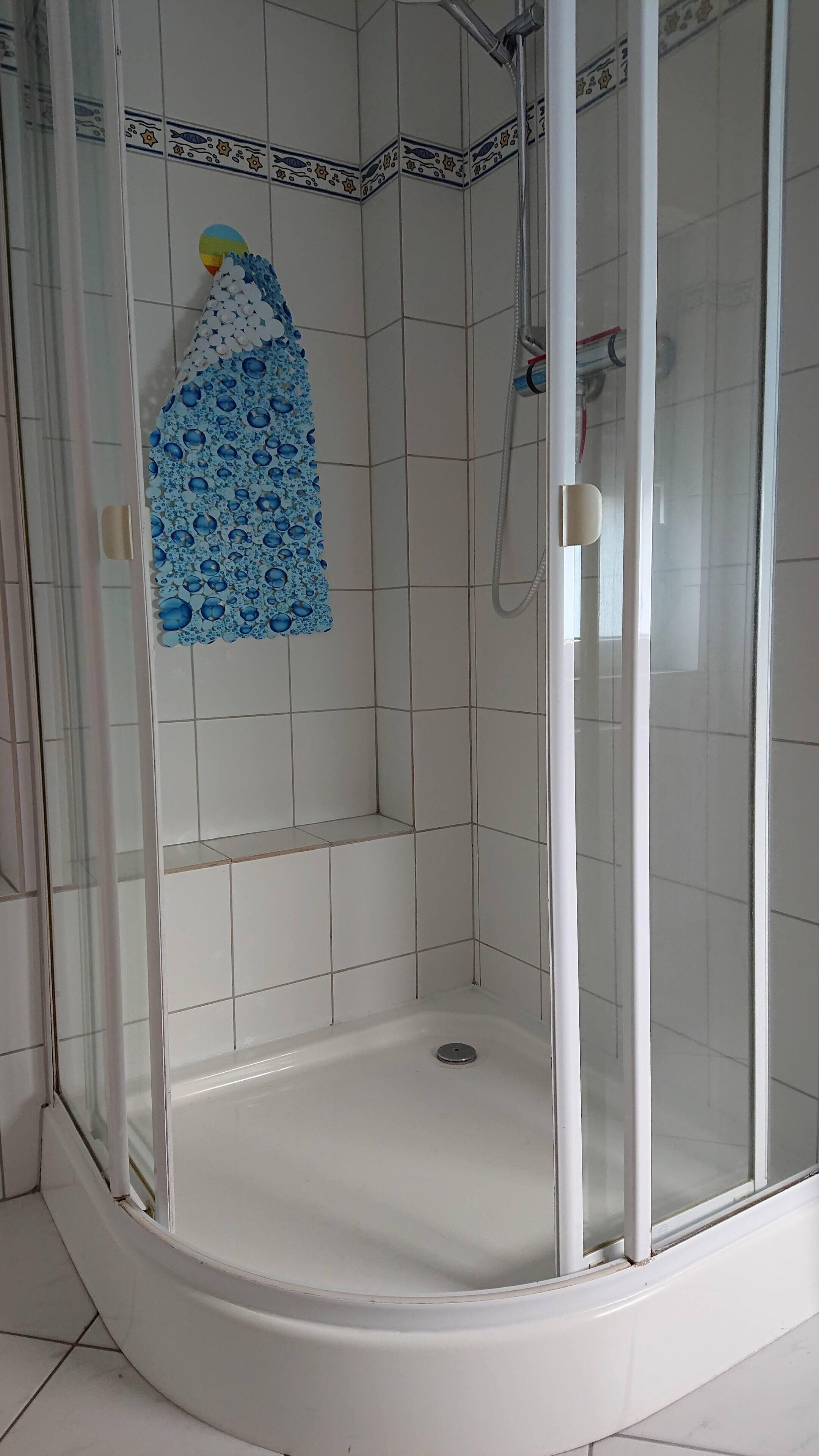 Eine Duschkabine mit Glas, weißen Fliesen und einem blauen Duschvorhang.