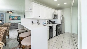 A modern kitchen with white cabinets, a microwave, a refrigerator, and a dishwasher. There are three stools at the kitchen island.